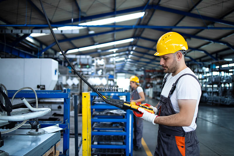 Operador com capacete e luvas utiliza o controle de uma máquina industrial.