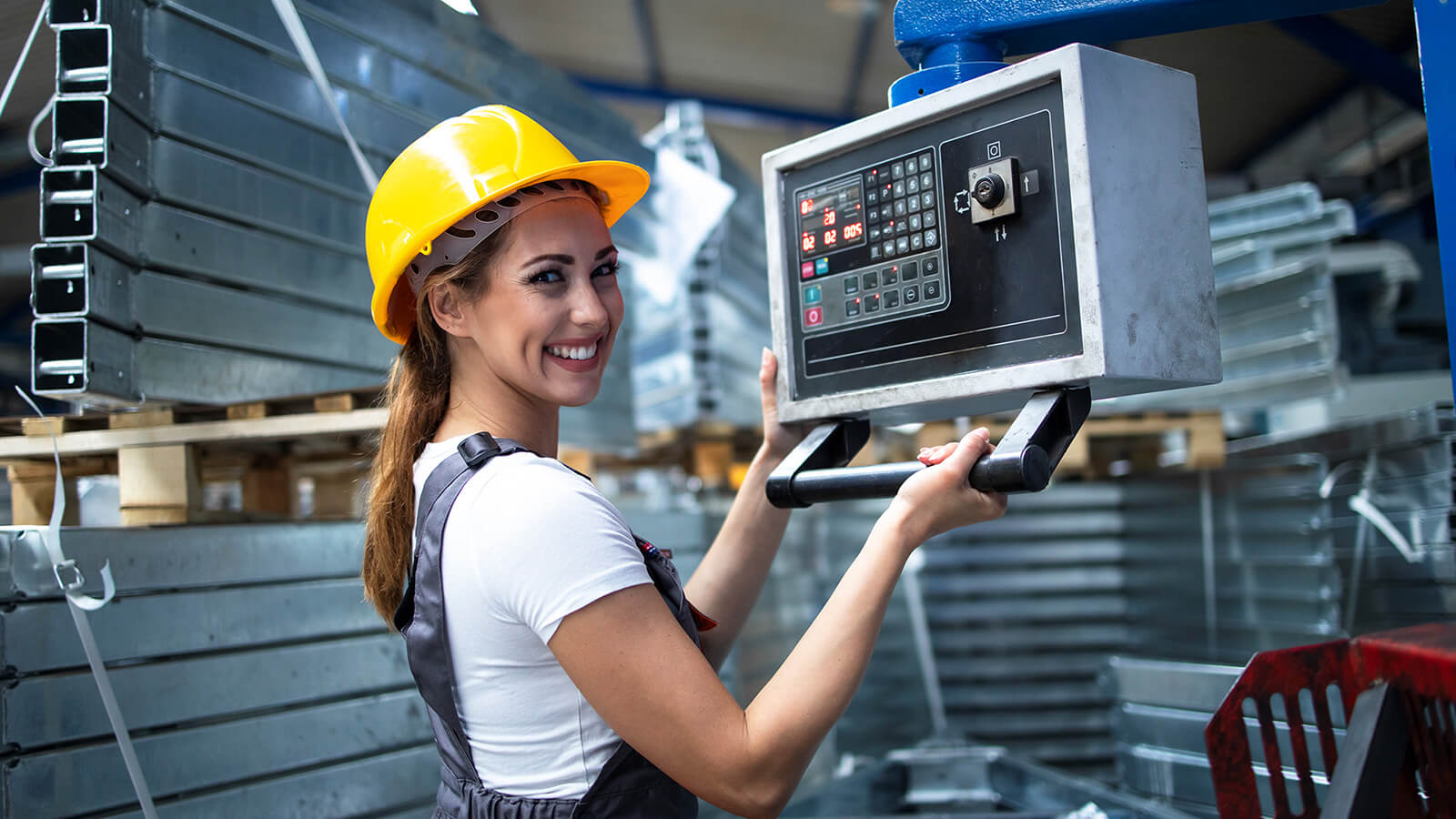 Operadora com capacete ao lado do painel de comando de uma máquina industrial.