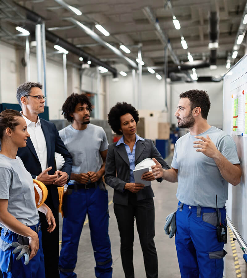 Profissional orienta uma equipe durante treinamento em ambiente industrial.