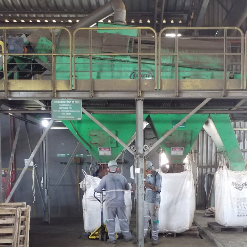 Trabalhadores operando equipamentos industriais em ambiente protegido por grades, necessitando de inspeção e manutenção conforme normas NR12.