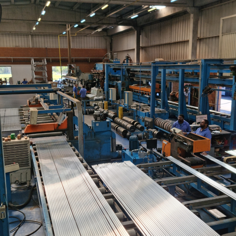 Vista detalhada de linha de produção industrial, com esteiras transportadoras e operadores em atividade, necessitando de inspeção e manutenção conforme normas NR12.