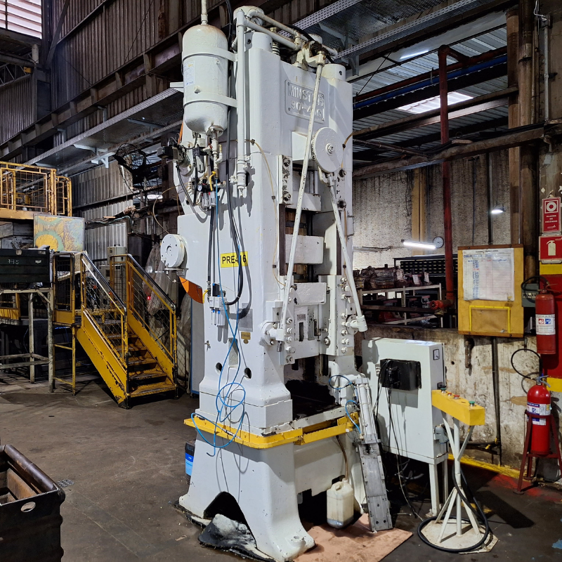 Vista detalhada de máquina industrial de estamparia, com componentes mecânicos e elétricos visíveis, necessitando de inspeção e manutenção conforme normas NR12.
