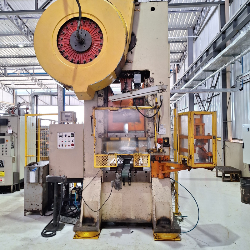 Vista detalhada de máquina industrial de estamparia com painel de controle e componentes mecânicos visíveis, necessitando de inspeção e manutenção conforme normas NR12.