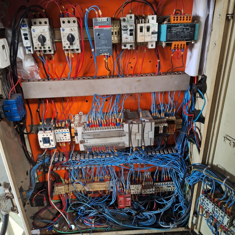 Vista detalhada de caixa de controle elétrico industrial com componentes eletrônicos organizados, necessitando de inspeção e manutenção conforme normas NR12.