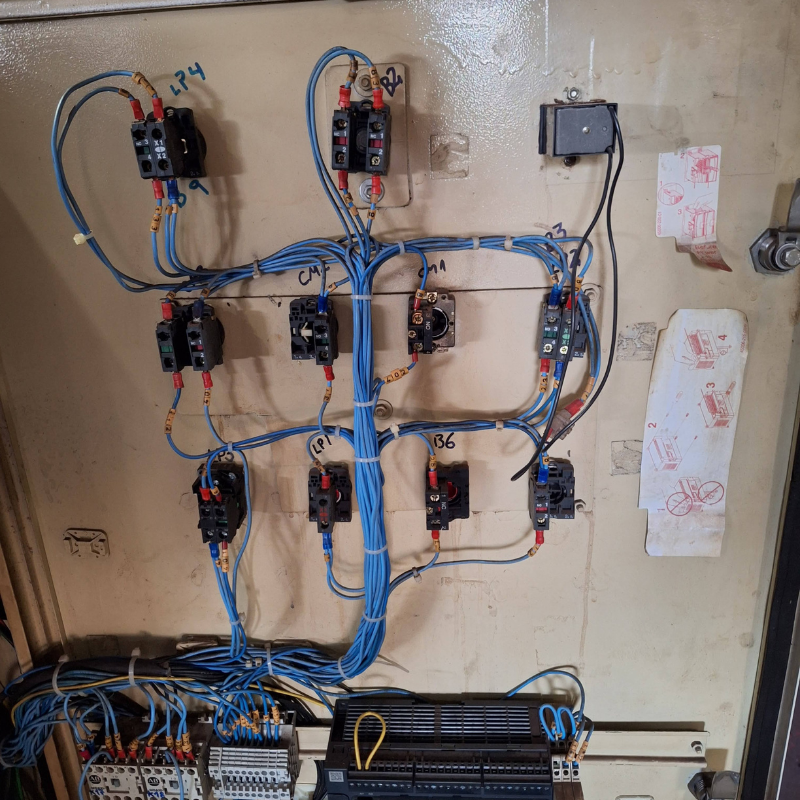 Vista detalhada de caixa de controle elétrico industrial com componentes eletrônicos organizados, necessitando de inspeção e manutenção conforme normas NR12.