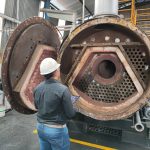 Profissional de engenharia utilizando tablet para inspecionar caldeira industrial aberta, seguindo as diretrizes da NR13.
