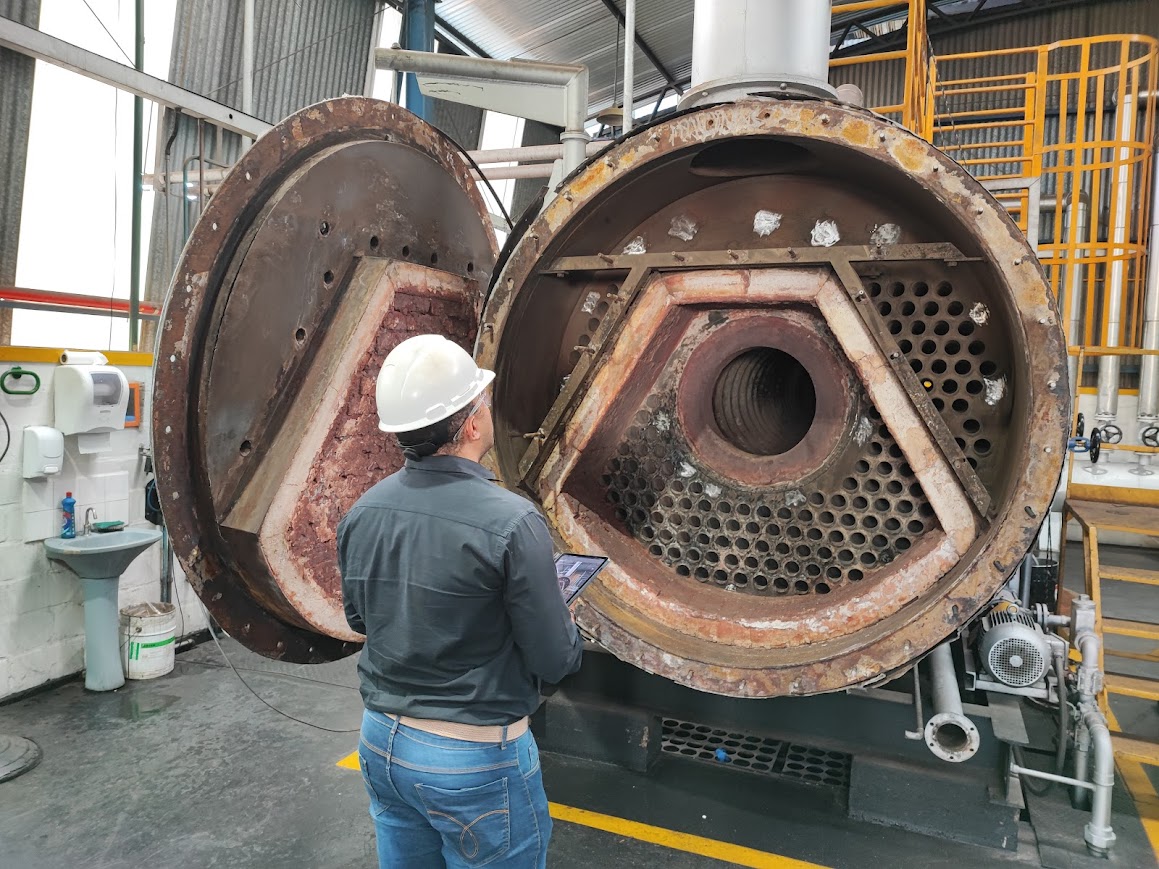 Profissional de engenharia utilizando tablet para inspecionar caldeira industrial aberta, seguindo as diretrizes da NR13.