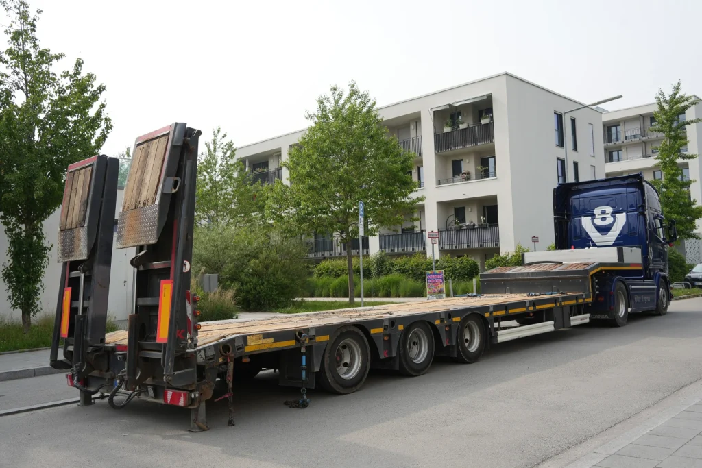 Caminhão-prancha vazio com duas rampas traseiras articuladas elevadas; fotografia ilustrativa de outro equipamento.
