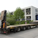 Caminhão-prancha vazio com duas rampas traseiras articuladas elevadas; fotografia ilustrativa de outro equipamento.