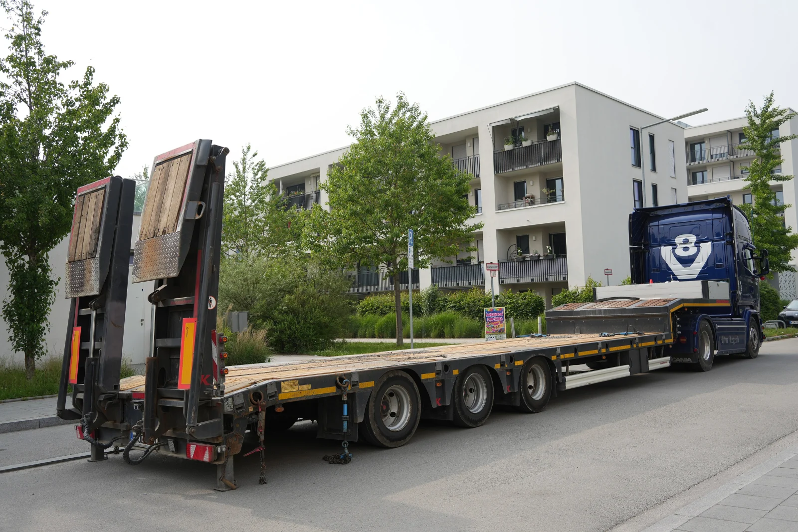 Caminhão-prancha vazio com duas rampas traseiras articuladas elevadas; fotografia ilustrativa de outro equipamento.
