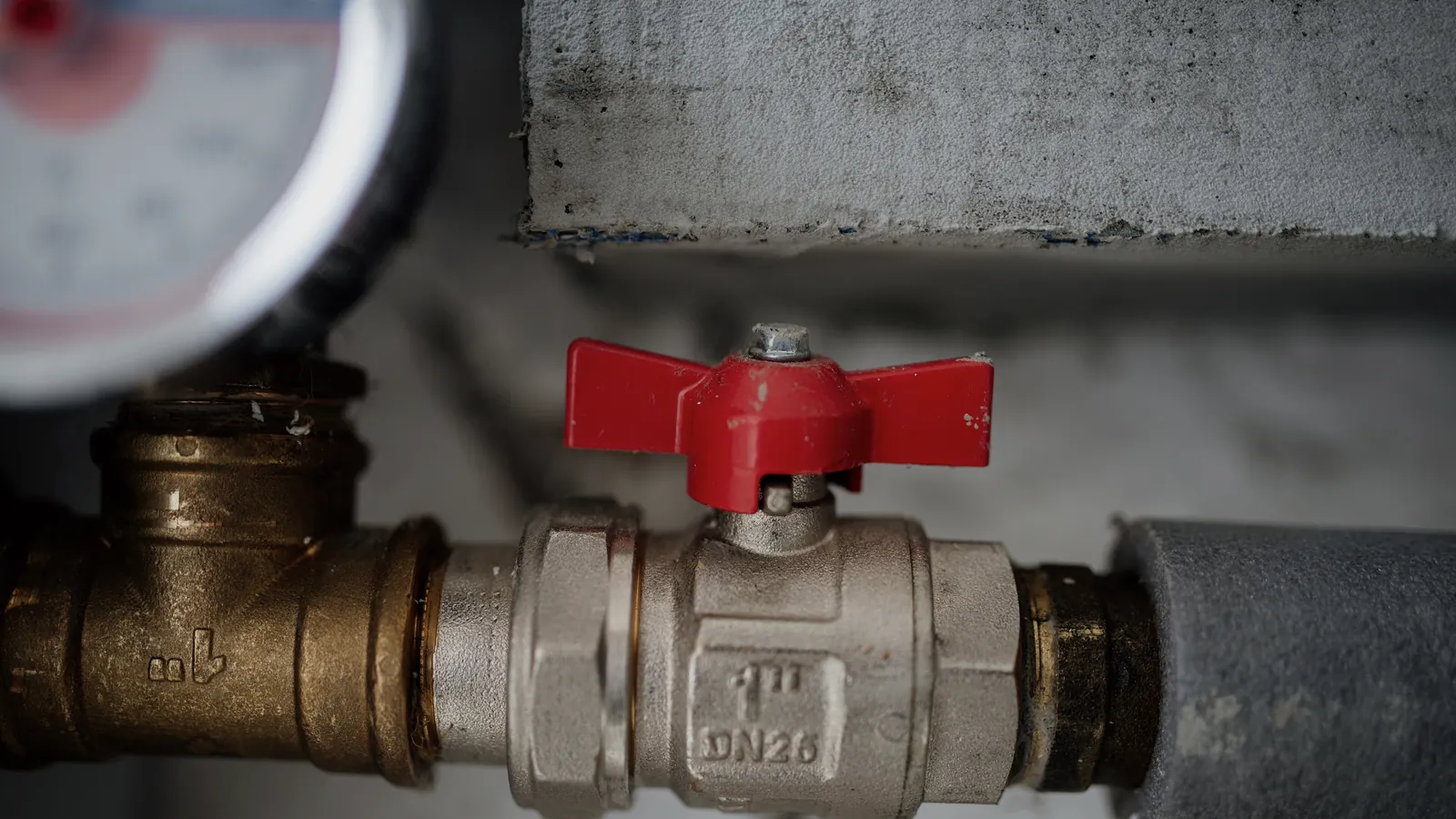 Válvula manual vermelha e manômetro instalados em trecho de tubulação metálica