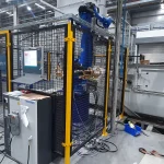 Célula robotizada cercada por proteção perimetral metálica amarela e preta