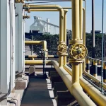Tubulações industriais amarelas e válvulas conectadas a equipamento de processo