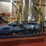 Sala de máquinas de refrigeração industrial com compressores e tubulações identificadas para amônia