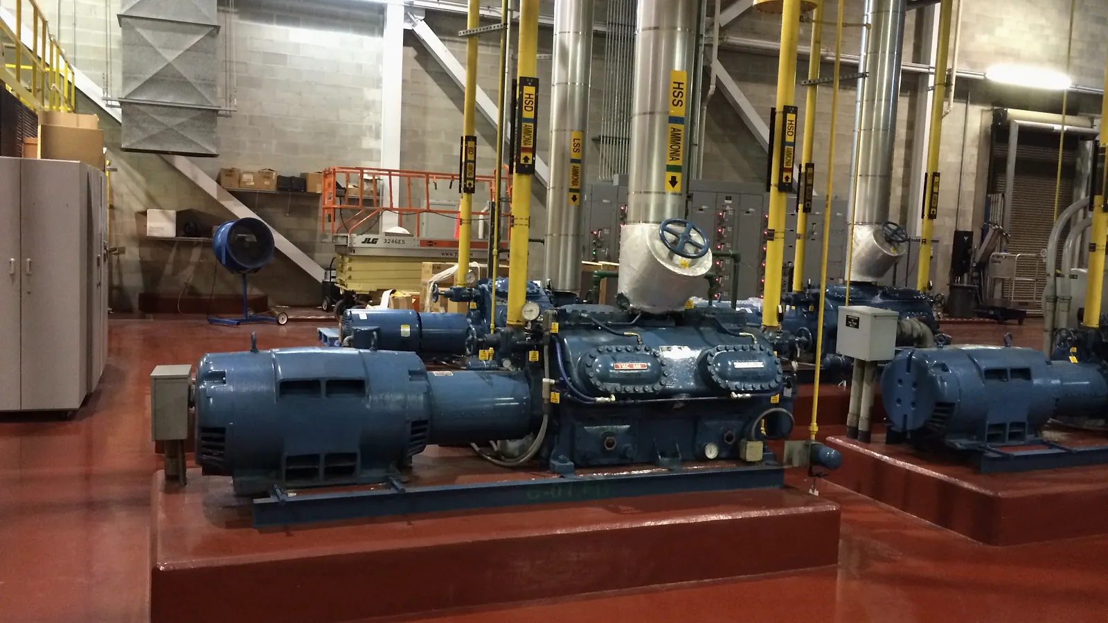 Sala de máquinas de refrigeração industrial com compressores e tubulações identificadas para amônia