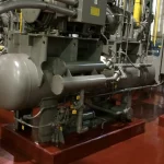 Unidade de compressão industrial com vaso de pressão horizontal em primeiro plano sobre base pintada