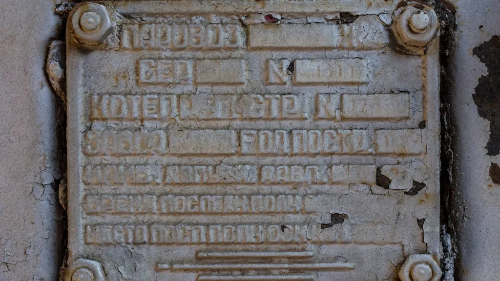 Placa metálica de identificação de caldeira fixada com parafusos, com letras em relevo parcialmente apagadas pela tinta e pela corrosão