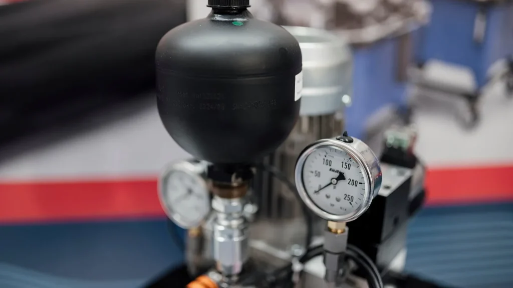 Pequeno vaso de pressão preto com dois manômetros de mostrador em unidade hidráulica exposta em feira industrial